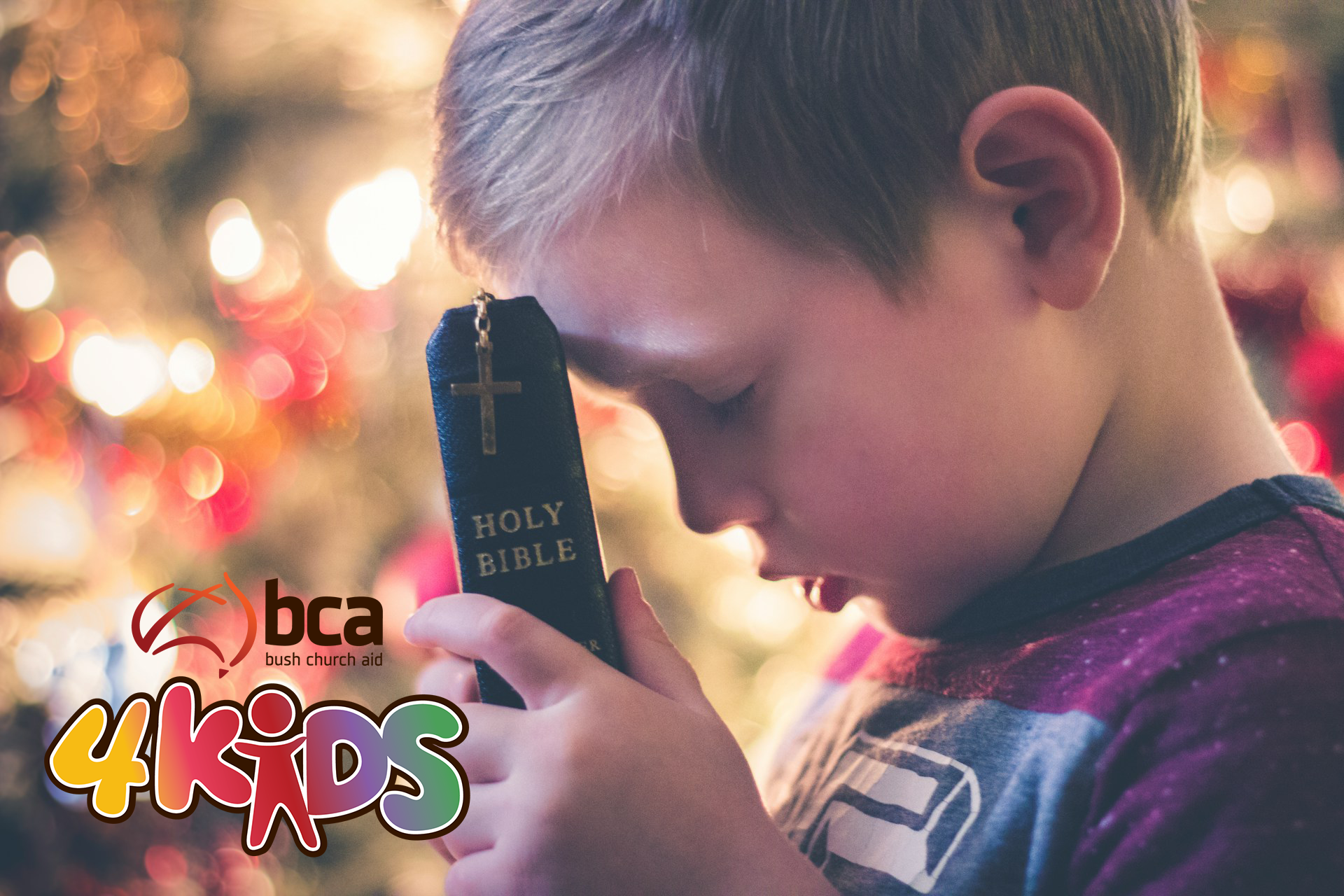 A boy holding a Bible to his forehead as he prays silently with eyes clodes